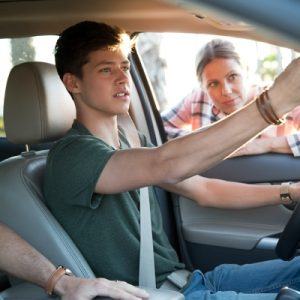 Young man adjust mirror from driver's seat while woman leans in through the window