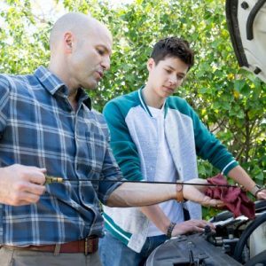 Man teaches boy how to check oil on a car