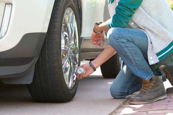 Man checking tire pressure on white car