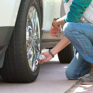 Man kneeling to check tire pressure on white car