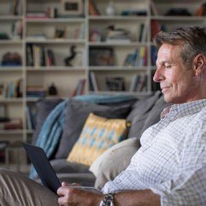 man sitting on couch looking at laptop