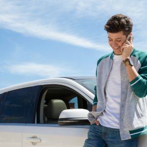 Young man standing beside car talking on cell phone