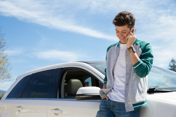 Young man standing beside car talking on cell phone