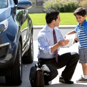 man kneeling to talk with his son beside car