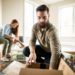 two people packing items into cardboard boxes
