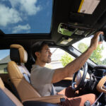 A man is sitting in the driver's seat of a car, checking his rearview mirror.