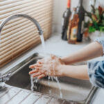 A woman washing her hands in the kitchen sink.