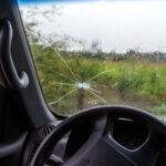 Rain washes over a cracked windshield.