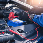 A mechanic wearing gloves as they work on a car battery.