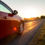 A red car drives down a country road at sunset.