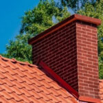 A red brick chimney sitting on top of a terra cotta tile roof.