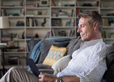 man sitting on couch looking at laptop