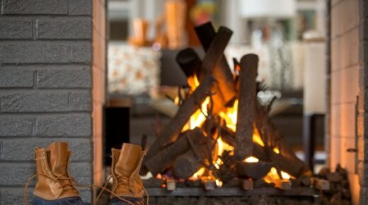 Brown duck boots sitting in front of a lit fireplace.