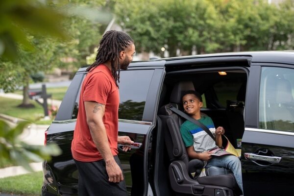 father outside of van with son buckled in seat