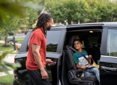 father outside of van with son buckled in seat