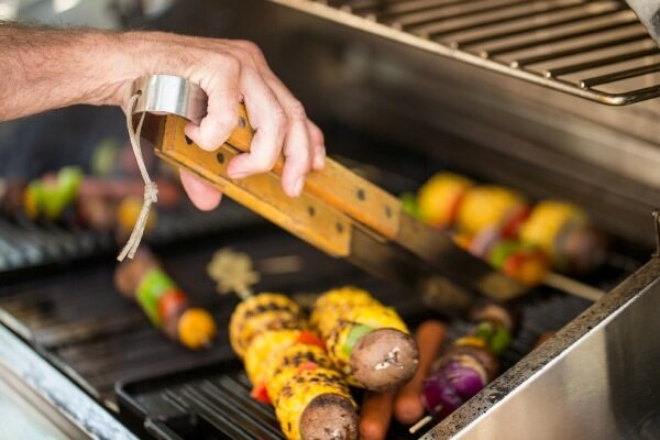 Person using grilling tongs to flip skewers on a grill.