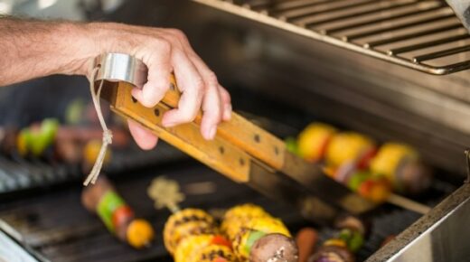 Person using grilling tongs to flip skewers on a grill.