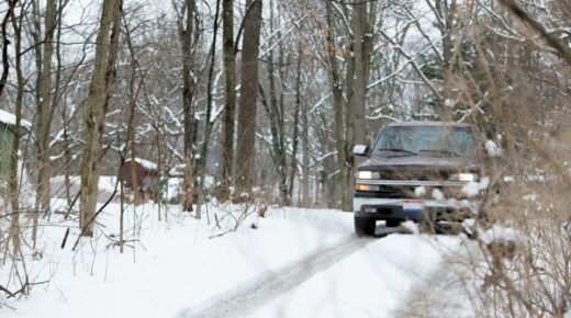 A truck driving on a snow-covered road in the woods.