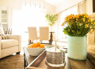 Living room table with a bowl of oranges and a vase of yellow flowers.