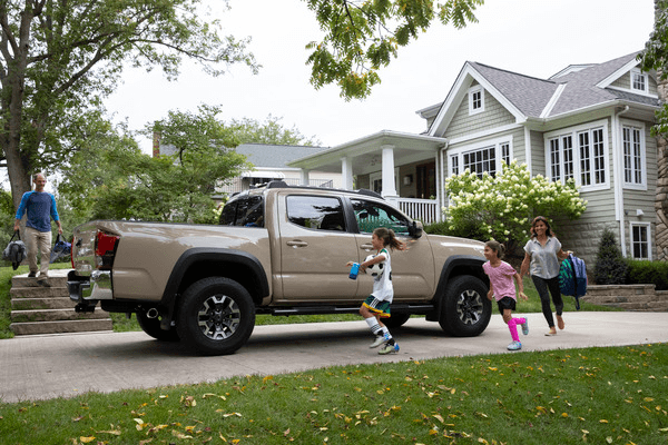 A family runs towards the car in the driveway.