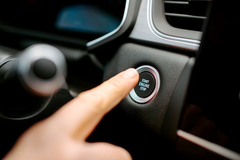 A finger pushing the start engine button in a car.