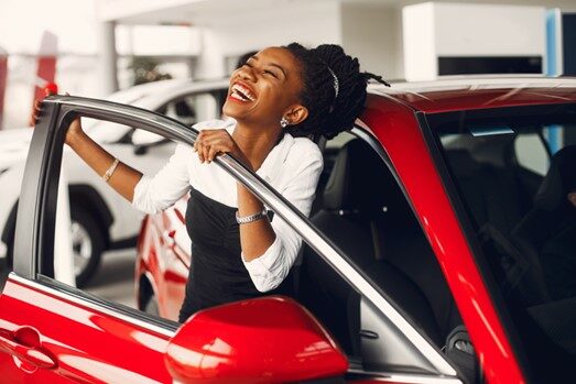 A woman smiling while leaning out of an open car door.