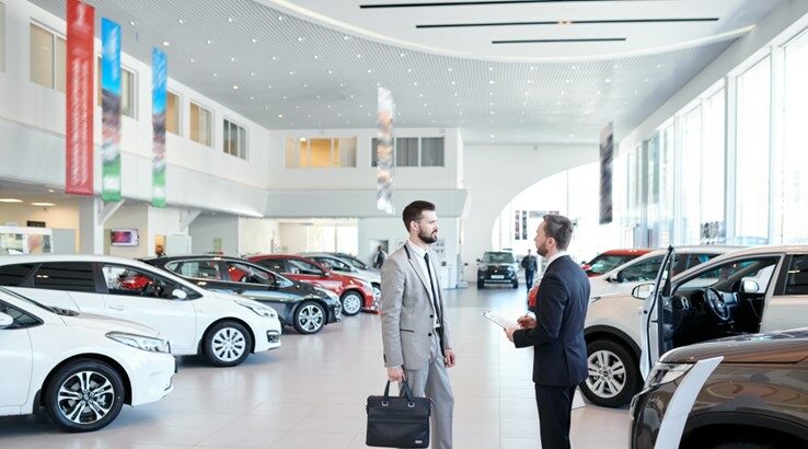 Two men standing in a car dealership.