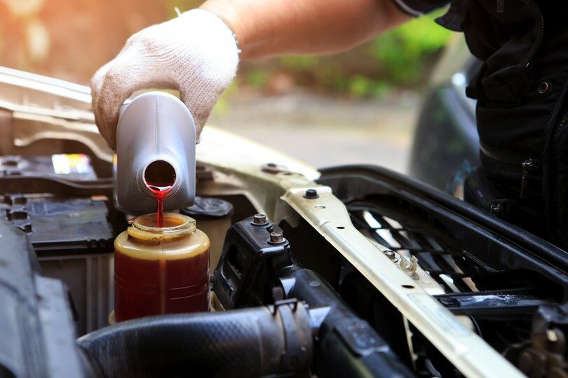 A person pouring fluid into a car’s engine.