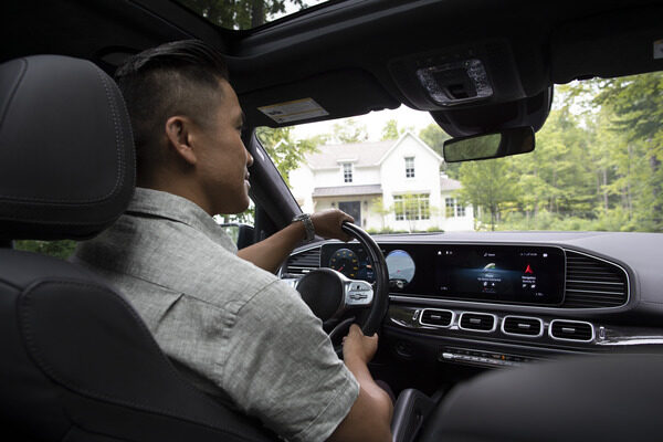 A dark-haired young man driving a car and looking in the rearview mirror.