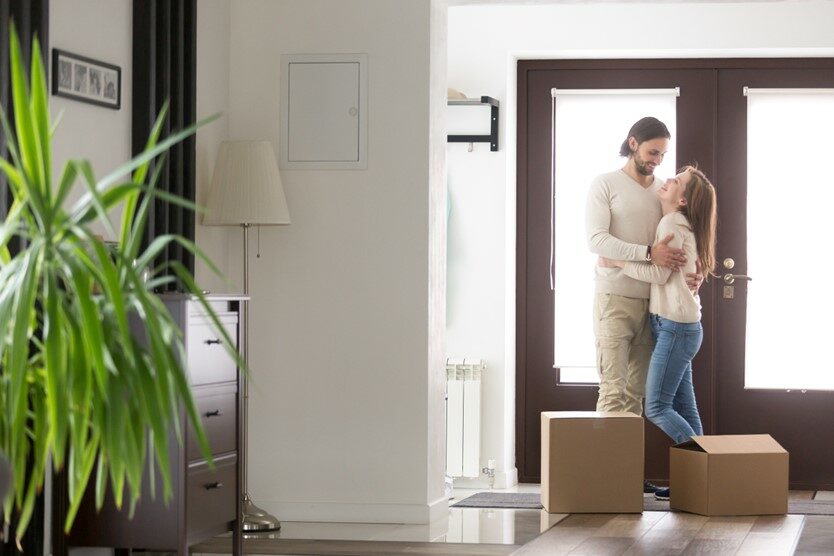 A young couple standing in a doorway of a home with moving boxes at their feet.