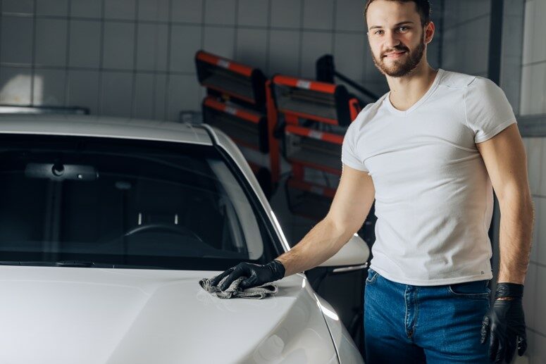 A man standing next to a car and waxing it.