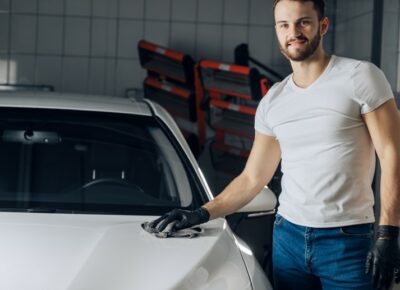 A man standing next to a car and waxing it.