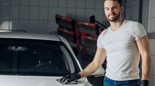 A man standing next to a car and waxing it.