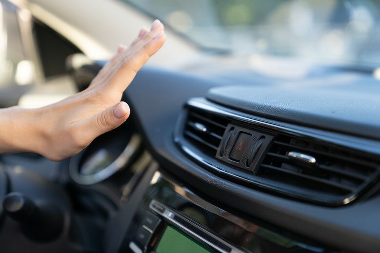 Hand reaching out to feel air from a car vent.