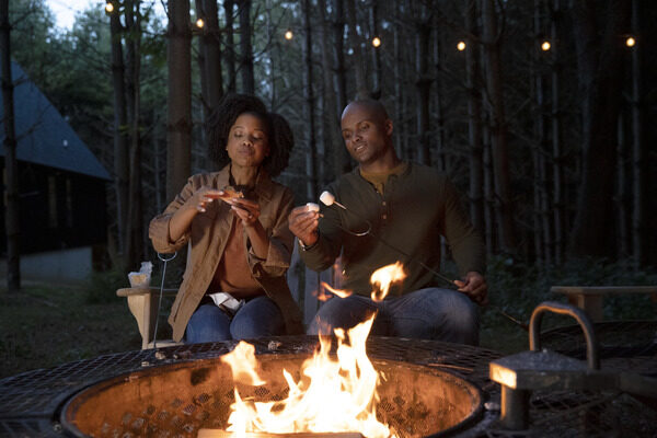 Two people sitting around a campfire and making smores.