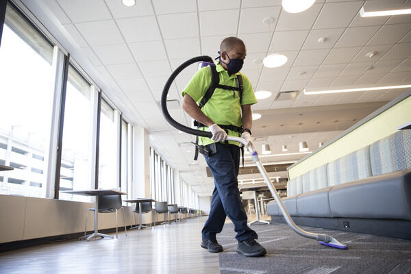 Person with a mask on their face as they vacuum carpet.