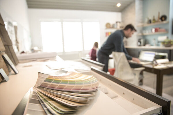 Paint swatches sitting on a desk while a man looks at his laptop