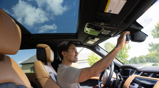 A man is sitting in the driver's seat of a car, checking his rearview mirror.