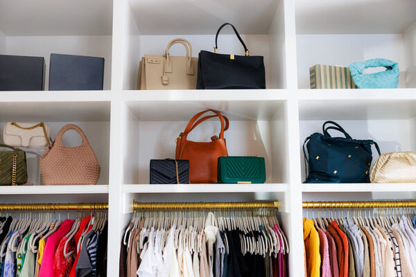 The inside of a closet with purses on the top shelves.