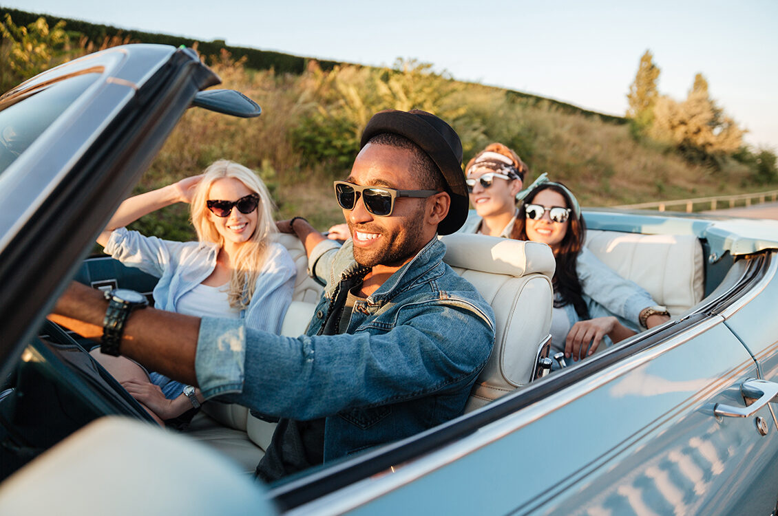 Man driving his friends in a convertible car.
