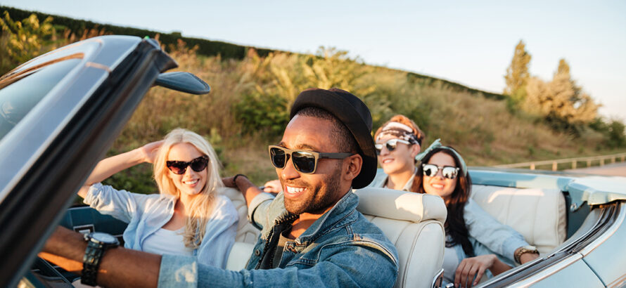 Man driving his friends in a convertible car.
