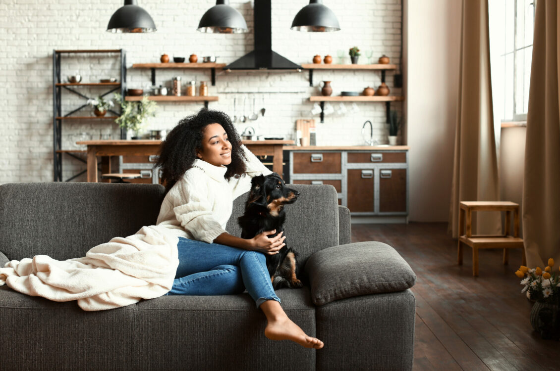 A woman petting a dog while both are sitting on the couch.