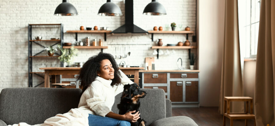 A woman petting a dog while both are sitting on the couch.