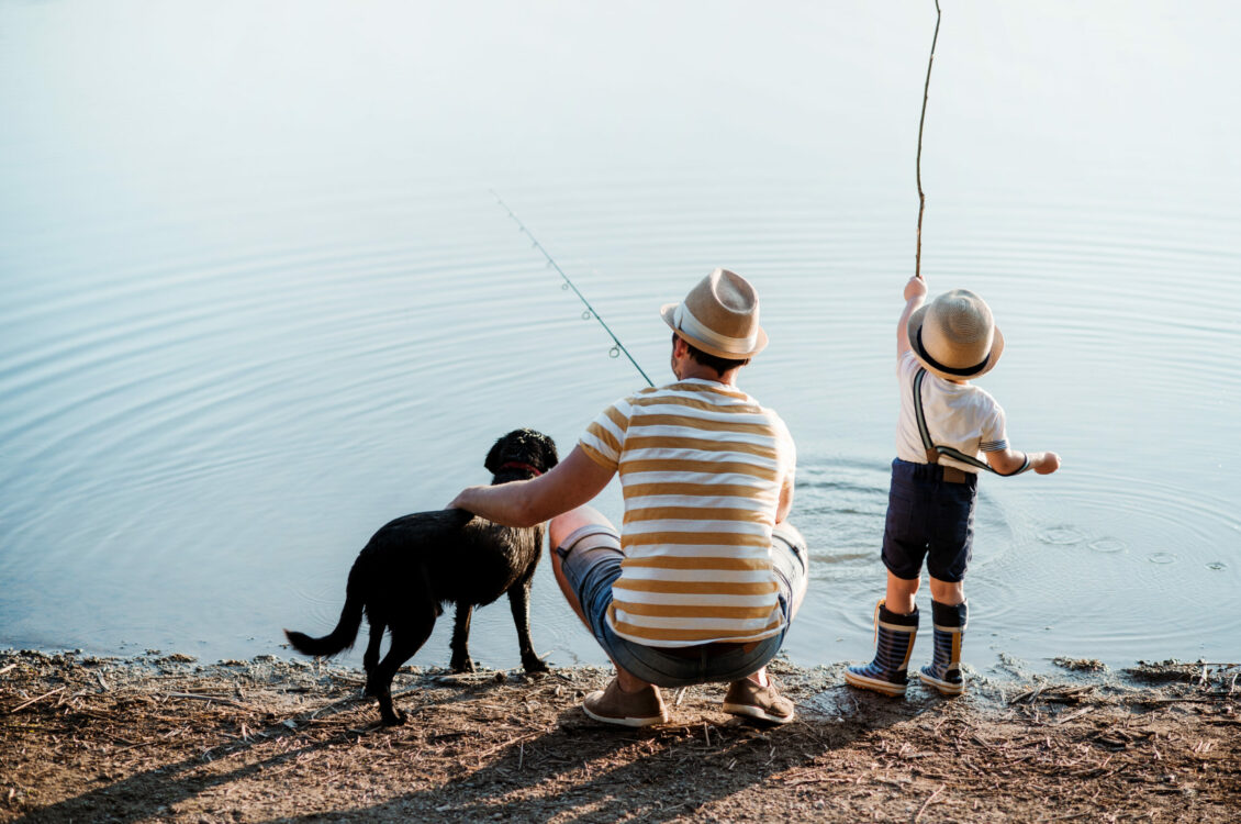 A man and a child doing fishing with a dog nearby them.