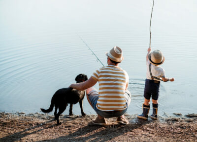 A man and a child doing fishing with a dog nearby them.
