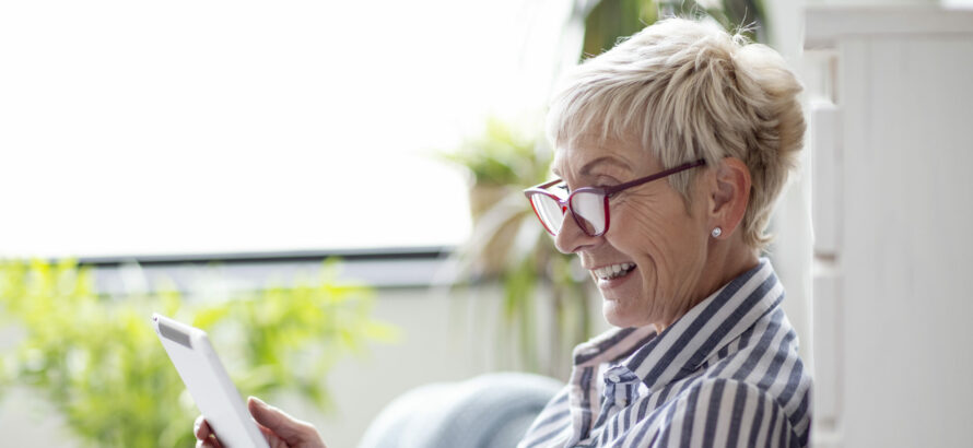 A happy woman using a tablet device while being outside of the house.