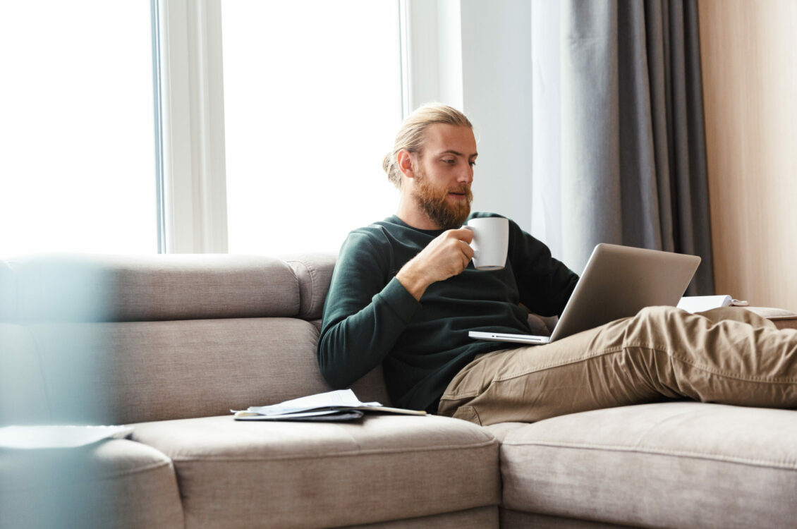 A man checking his laptop while holding a mug.