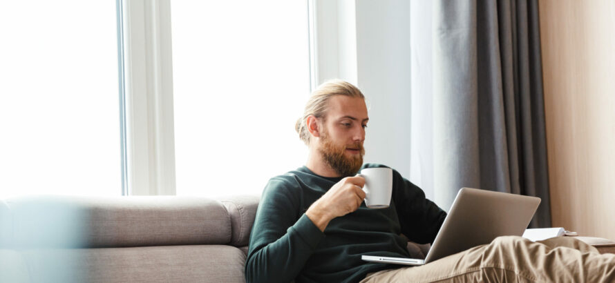 A man checking his laptop while holding a mug.