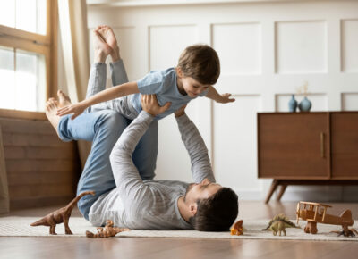 A man laying on his back and lifting a child in the air at home.