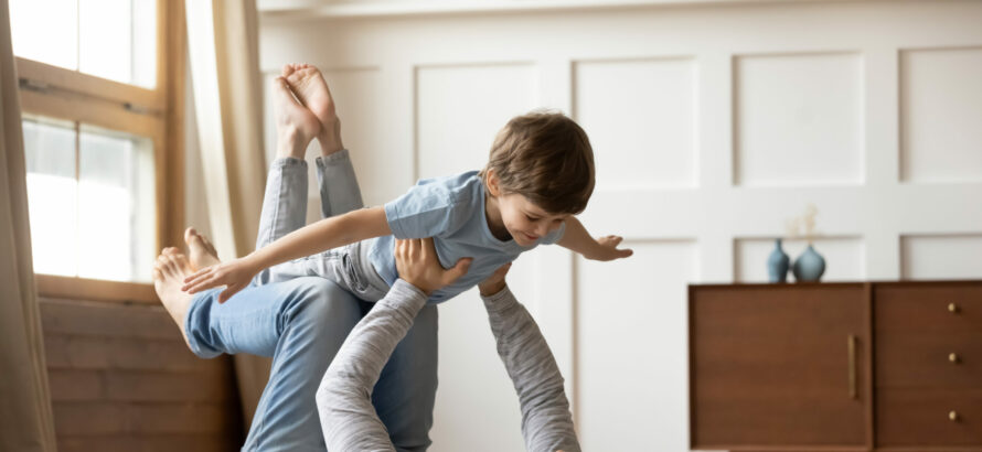 A man laying on his back and lifting a child in the air at home.